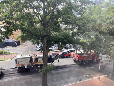 The white truck grinds up the asphalt layer and spits it out into the red truck.